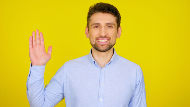 Knappe man met baard in een lichtblauw shirt verwelkomt met een handpalm en glimlacht - Foto, afbeelding