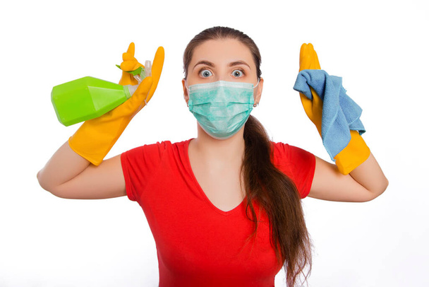 Young woman in mask and gloves holds spray bottle and rag isolated on a white background. Cleaning the house and premises, the prevention of viral diseases. - Fotó, kép