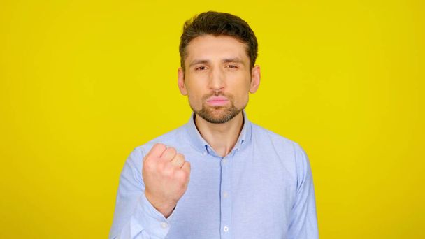 Angry man shows fist on a yellow background with copy space - Photo, Image