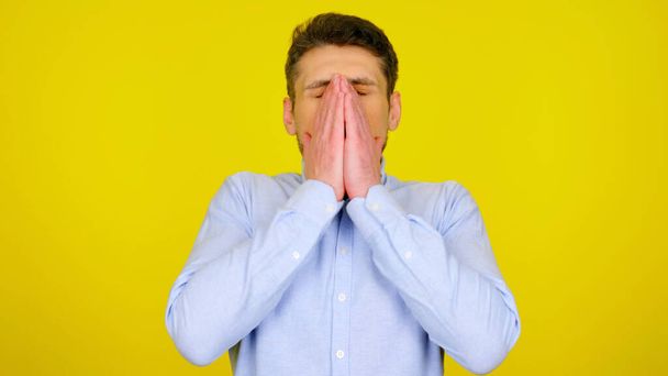 Sick man sneezes covering face with hands on a yellow background with copyspace - Фото, изображение