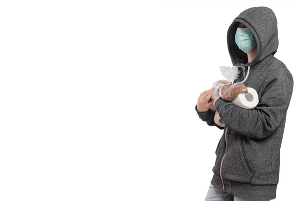 コロナウイルスパニック、フード付きのスウェットシャツの少女、マスクの概念は、シリアル、そば、米とトイレットペーパーとパッケージのロールを運ぶ。白い背景に隔離された. - 写真・画像