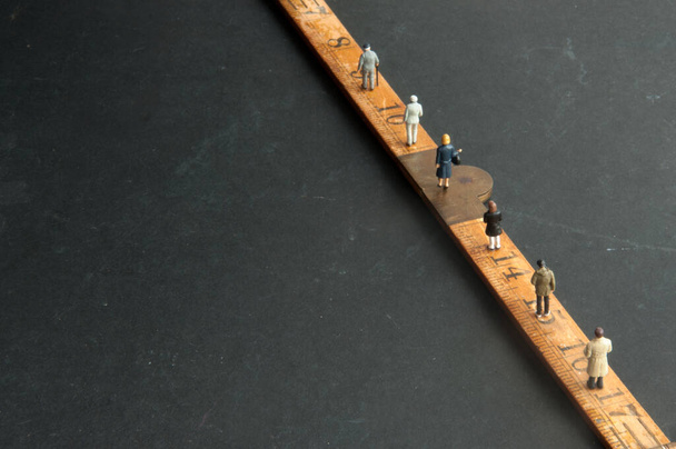 Social distancing coronavirus queue of miniature people walking on a ruler on top of a chalkboard - Photo, image