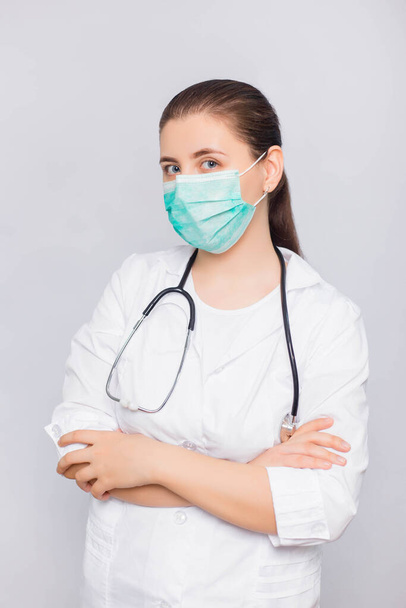 Doctor girl in a white coat and medical mask with a stethoscope isolated on white background. - Fotó, kép