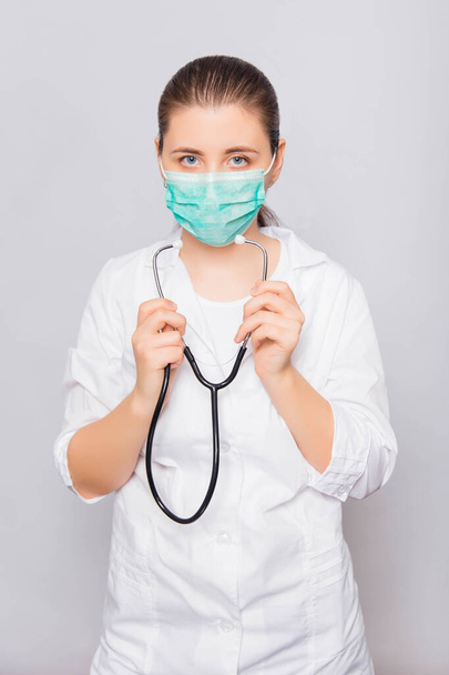 Doctor girl in a white coat and medical mask with a stethoscope isolated on white background. - Φωτογραφία, εικόνα