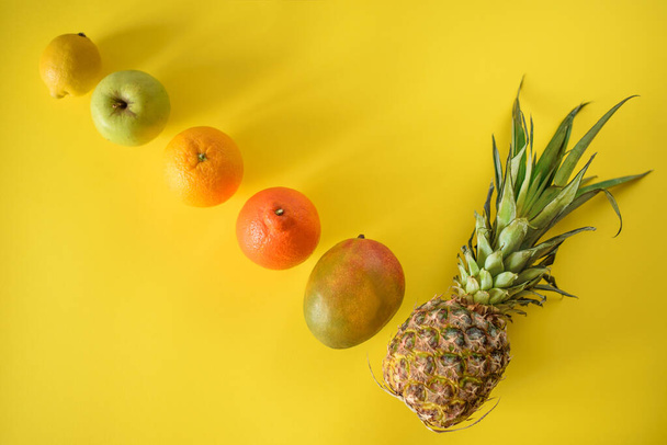 Draufsicht auf ganze runde tropische Früchte, die diagonal auf gelbem Hintergrund liegen, von klein bis groß - Foto, Bild