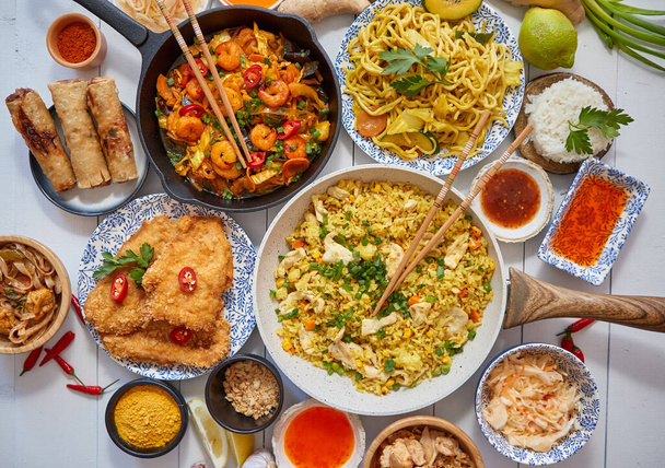 Comida asiática servida. Platos, sartenes y tazones llenos de fideos salteados de pollo y verduras - Foto, Imagen