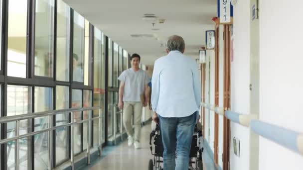 twee vriendelijke aziatische artsen begroeten senior patiënten tijdens het lopen praten in het ziekenhuis hal - Video