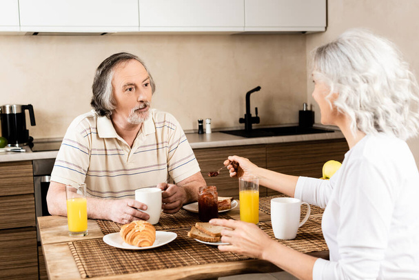 selective focus of bearded and mature man looking at wife near tasty breakfast  - Foto, immagini