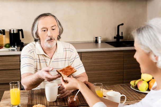 selective focus of mature woman giving sweet toast bread with jam to husband  - 写真・画像