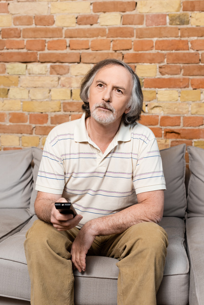 Älterer Mann hält Fernbedienung in der Hand, während er Film zu Hause anschaut  - Foto, Bild
