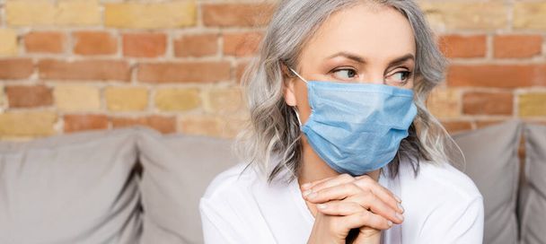 horizontal image of mature woman in medical mask with clenched hands  - Photo, Image