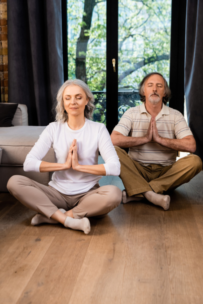 relaxed mature couple with closed eyes and praying hands sitting in lotus pose  - Fotografie, Obrázek