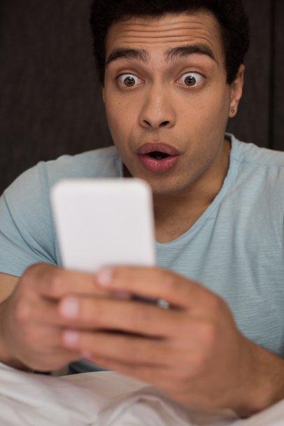 шокований молодий змішаний гоночний чоловік використовує смартфон, вибірковий фокус
 - Фото, зображення