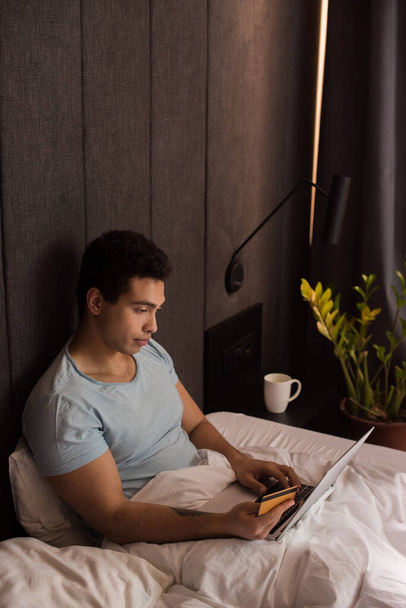 beau mixte homme de course shopping en ligne avec carte de crédit et ordinateur portable au lit en quarantaine
 - Photo, image