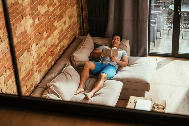 mixed race man reading book while chilling on sofa during quarantine - Photo, Image