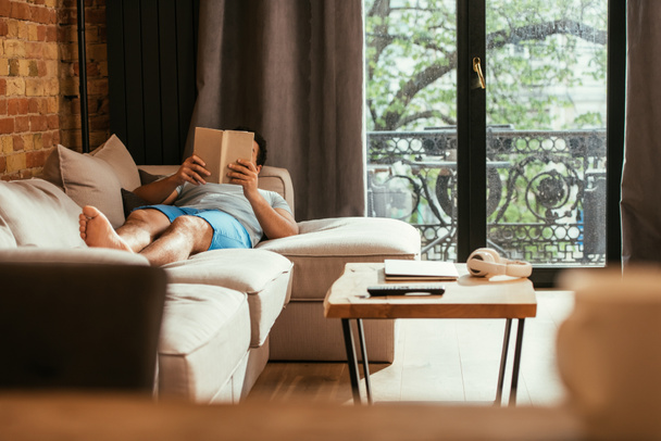 young man reading book while lying on sofa during quarantine - Photo, image