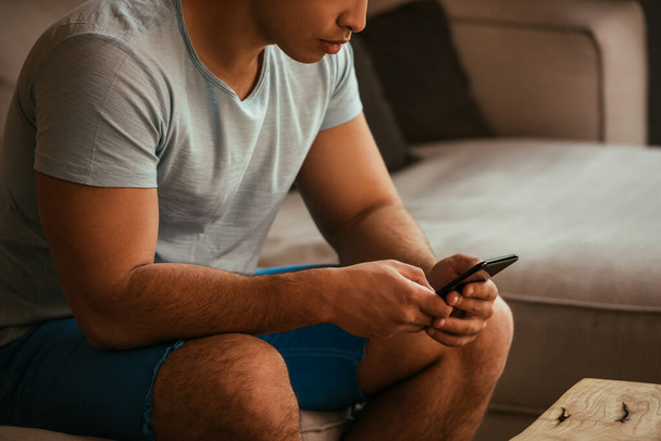 cropped view of young man using smartphone on sofa during self isolation  - Foto, Bild