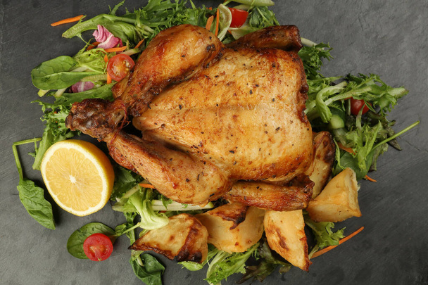 Celé pečené grilované kuřecí drůbež pták s pečenými brambory zeleninový salát rajčatový citron na černé břidlice kámen řezání deska černé pozadí - Fotografie, Obrázek