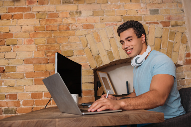 glimlachende gemengde ras freelancer werken met laptop in huis kantoor tijdens zelfisolatie - Foto, afbeelding