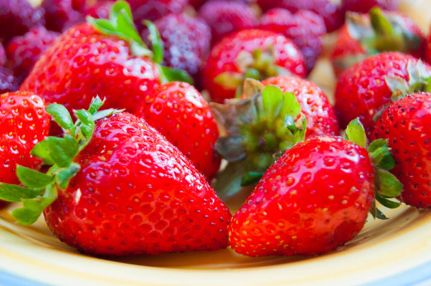 夏の熟した果実とプレート-イチゴ、イチゴ、ラズベリー。ビタミンおいしいシンプルな自然ビーガンジューシーなデザート.夏の香り。暖かい日差しの中でベリー. - 写真・画像