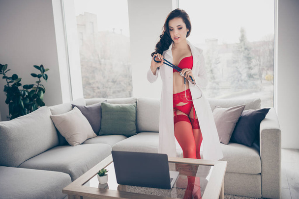 Photo of tempting slim lady work home private online notebook chat undressing nude body play naughty bad nurse role look screen flirty wear lab coat red bikini tights room indoors - Foto, afbeelding