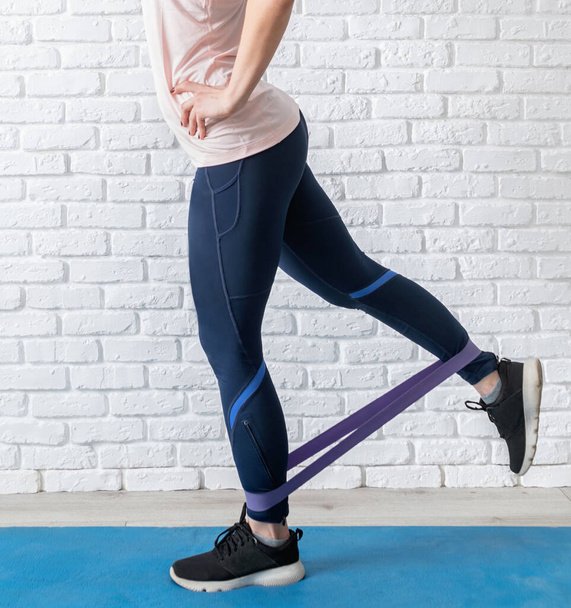 Quédate en casa. Fitness en casa. Una mujer ejercitando las piernas en casa usando goma banda de resistencia
 - Foto, Imagen