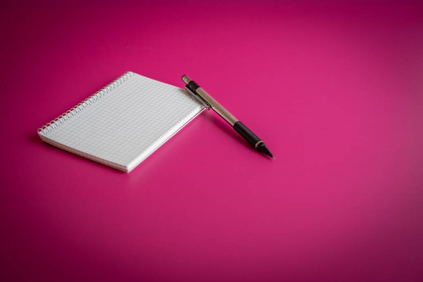 Geruit notitieboekje met pen op fuchsia achtergrond - Foto, afbeelding
