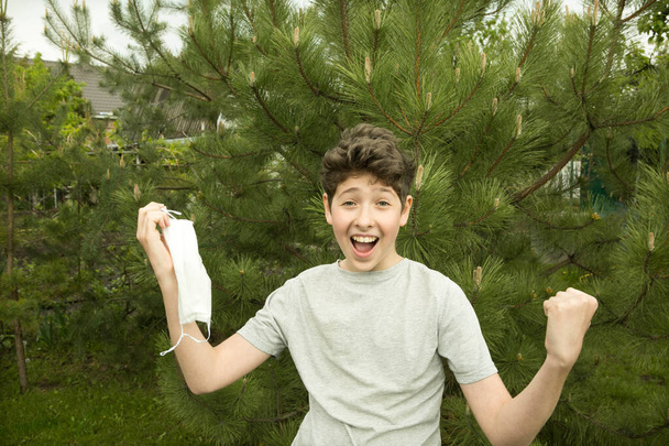 Η χαρά ενός νεαρού άντρα στη φύση μετά την καραντίνα. Το αγόρι βγάζει τη μάσκα του και αναπνέει καθαρό αέρα.. - Φωτογραφία, εικόνα