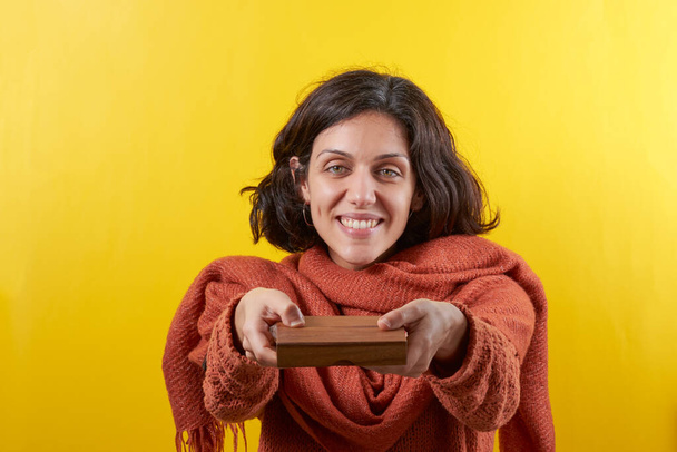 Γυναίκα προσφέρει ένα μικρό ξύλινο κουτί. Το φόντο είναι κίτρινο.. - Φωτογραφία, εικόνα