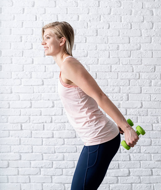 Stay home. Home fitness. Smiling young woman exercising with dumbbells at home - Photo, Image