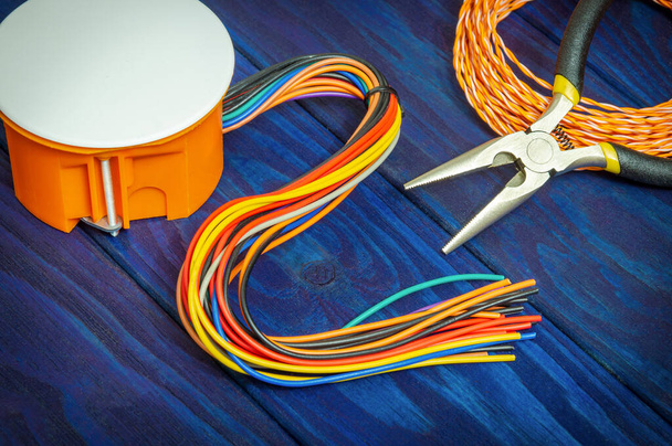 Caja anaranjada de unión eléctrica con alambres y herramientas en tableros de madera azul generalmente utilizados en el proceso de instalación eléctrica
 - Foto, imagen