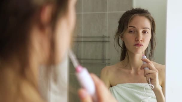 young girl brushes her teeth with an irrigator looking in reflection in the mirror close up - Filmagem, Vídeo