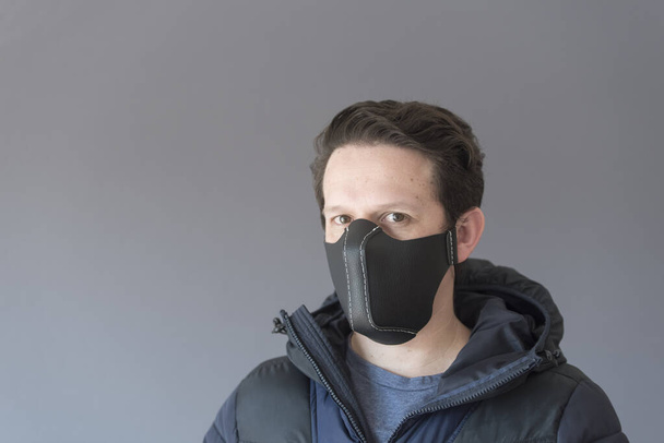Coronavirus 'un salgını bağlamında yayılmasını önlemek için ev yapımı sentetik deri maske takan genç bir adamın portresi. Ceket giyiyor, kışlık giysiler. - Fotoğraf, Görsel