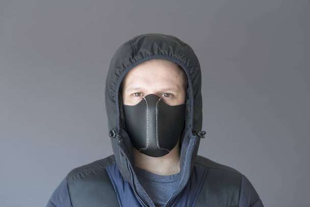Retrato de um jovem vestindo uma máscara de proteção de couro sintético caseiro, para evitar a propagação do coronavírus, no contexto do surto de covid-19. Ele está usando um casaco, roupas de inverno
 - Foto, Imagem