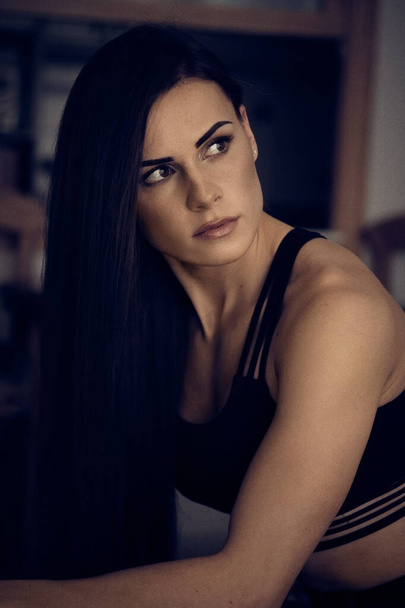Serious Caucasian 30s woman wearing black sporty top modern comfort activewear sitting posing indoors looking away. Concept of sporty healthy female athletic lifestyle, beauty and fashion - Fotó, kép