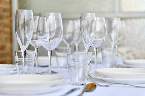 Close up new diverse of glassware and porcelain plates served on white tablecloth, no people. Table settings wait for guests at home or restaurant. Dinner party, tableware shop advertisement concept - Zdjęcie, obraz
