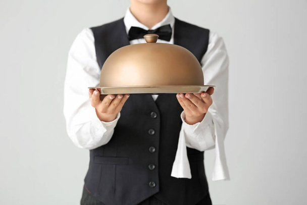 Hermosa camarera femenina con bandeja y cloche sobre fondo gris
 - Foto, Imagen