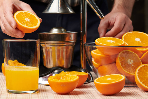 Squeezing an orange with a manual press, close view, making a glass of fresh. Fresh oranges on a wooden table, whole, squeezed and sliced. - Photo, Image