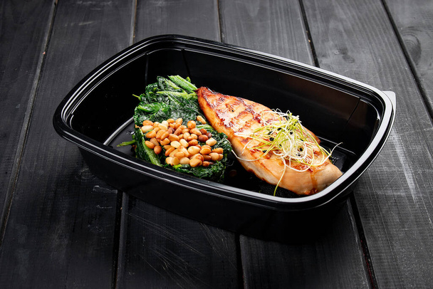 Chicken fillet with spinach and pine nuts in containers on a black wooden background. Takeaway. Diet and healthy food. - Fotoğraf, Görsel