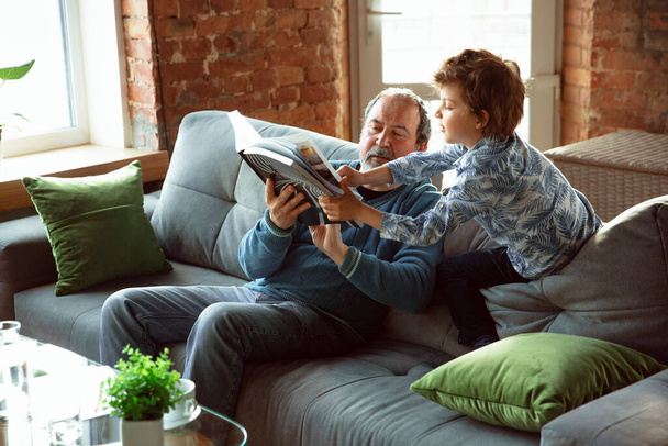 Großvater und Enkel verbringen Zeit isoliert zu Hause, haben Spaß, lesen gemeinsam Magazin, sind glücklich - Foto, Bild