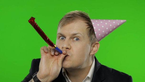 Drunk disheveled young businessman in festive cap celebrates, blowing a whistle - Photo, Image