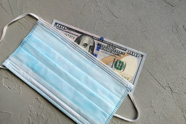 One hundred dollar bill and medical masks lie on the background. Finance and analytics in the era of the Corona virus. Biological concept of life in a new reality. Surgical ear mask and Money. - Photo, Image