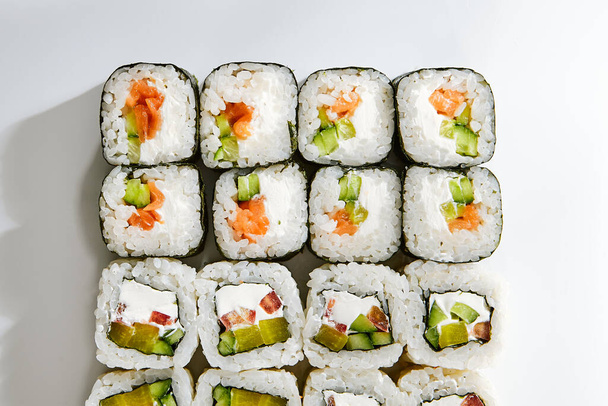 Roll set on white background top view. Delicious sushi, asian cuisine meal, healthy nutrition close up. Traditional japanese food, rice and fish dish with cucumber decoration, restaurant meal - Foto, afbeelding