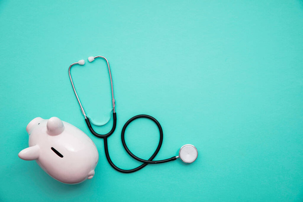 Cost of healthcare. Piggy bank money box with a medical doctors stethoscope - Zdjęcie, obraz