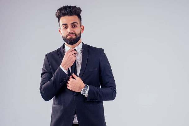 young turkish handsome black hair man in stylish business suit knotting the tie in studio isolate white background - Foto, immagini