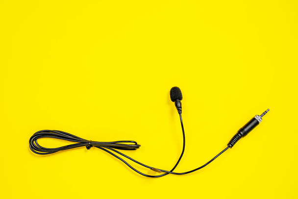 Lapel microphone with a bundled cord on yellow background, top view. Essential vlogging and journalism tools. - Foto, immagini