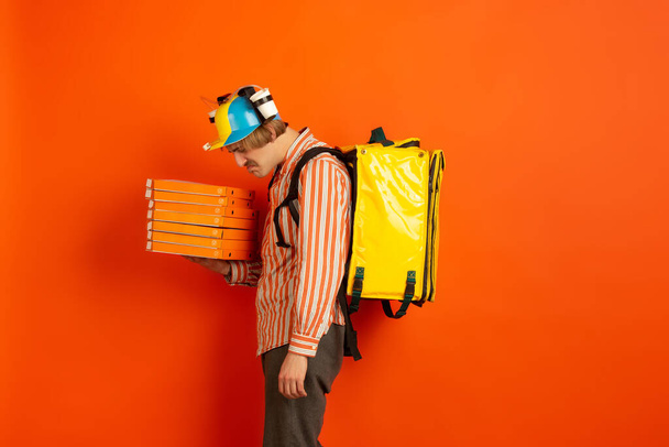 Contacless delivery service during quarantine. Man delivers food and shopping bags during insulation. Emotions of deliveryman isolated on orange background. - Foto, imagen