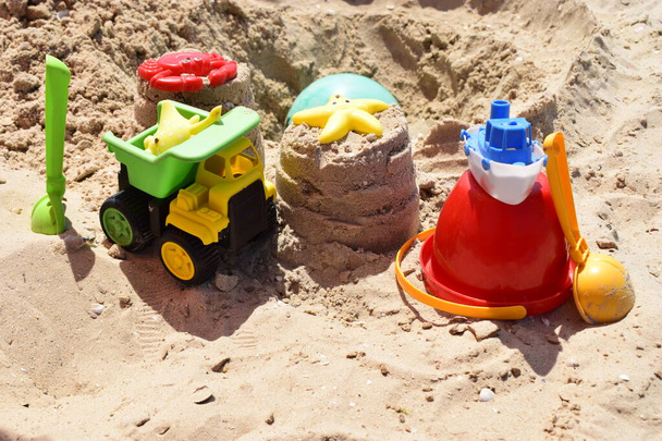 Plastikowe zabawki dla dzieci zielony koniec żółty samochód, łopata, czerwone wiadro, zielona kula z żółtym piaskiem na plaży nad morzem. Dziecięcy plażowy zabawka na piasek w słoneczny dzień. Piaskownica na placu zabaw dla gier - Zdjęcie, obraz