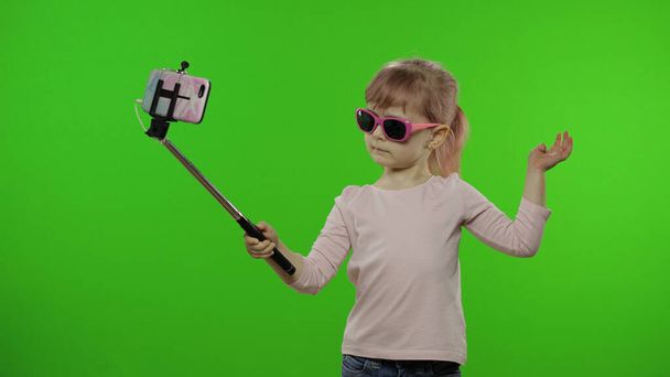 Menina criança faz selfie, blogging no telefone móvel usando vara selfie. Chave Chroma
 - Foto, Imagem