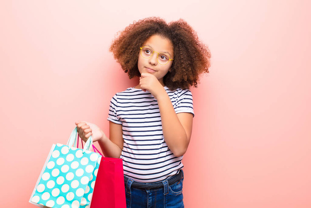 african american little girl  against flat wall with shopping bags - 写真・画像